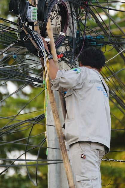 A close-up shot of a technician installing fiber optic cables in a rural area. The cables are brightly colored, and the backdrop shows rolling hills and scattered houses, highlighting the expansion of broadband internet access to underserved communities.