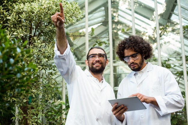 A diverse group of farmers and agricultural scientists discussing data on a tablet in a modern greenhouse, showcasing collaboration and technological adoption.