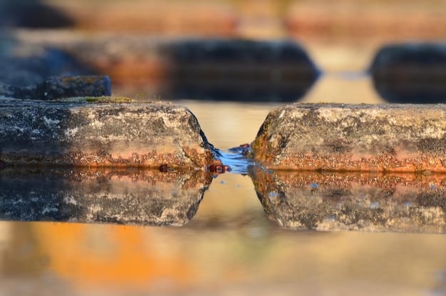 Close-up of a corroded and leaking underground water pipe, with water visibly escaping into the surrounding soil.