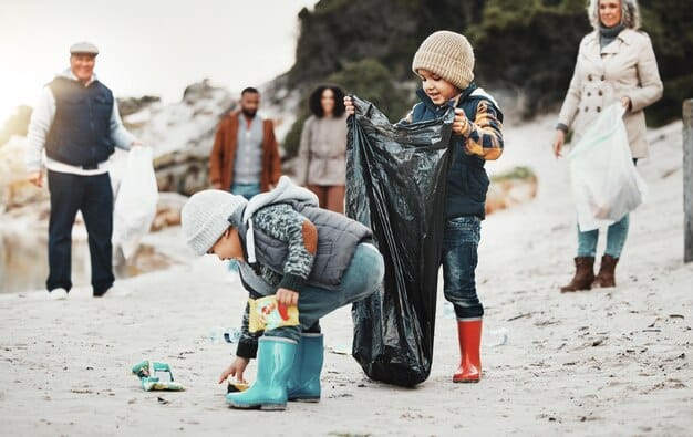 A diverse group of people participating in a community clean-up event, picking up plastic waste from a park or beach, with visible recycling bins.