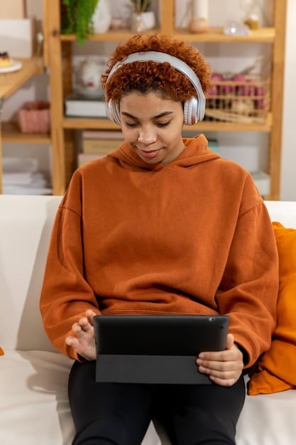 A student wearing headphones while participating in an online UX/UI design course on a tablet. The screen shows a design tutorial with colorful graphics and text. The setting is a cozy coffee shop with other people working around. This image underlines the versatility of online education resources for How to Become a UX/UI Designer in 2025: A Practical Guide.